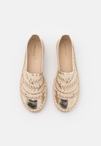 Espadrillas beige con punta metallica dorata, caratterizzate da motivi a foglia ricamati e una suola in juta intrecciata. Design semplice senza chiusure.
