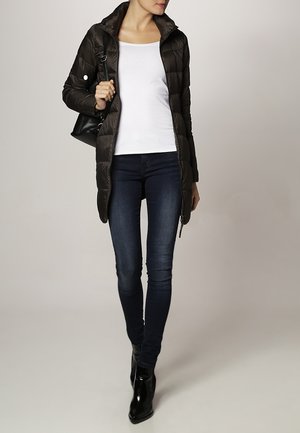 Black padded coat with a high collar, paired with a white long-sleeve shirt and dark blue skinny jeans. Black ankle boots and a small bag.
