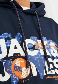 Sudadera azul marino con un diseño gráfico que presenta un globo en azul y naranja, adornada con cordones naranjas en contraste y herrajes plateados.
