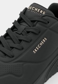 Černé tenisky Skechers s silnou podrážkou, texturovaným podešví, černými tkaničkami a logem "Skechers Los Angeles" na jazyku a na boku.