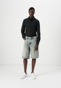 Camisa negra de manga larga con botones combinada con pantalones cortos de mezclilla azul claro de corte relajado y zapatillas blancas. Diseño minimalista, sin patrones.
