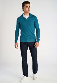 Jasnoniebieski dzianinowy polo z długim rękawem i kołnierzykiem, zestawiony z ciemnymi spodniami i białymi trampkami. Prosty design, dopasowany krój, gładka faktura.