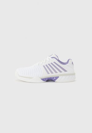 Hvid og lilla sports-sneaker med tekstureret tå, ventilationsåbninger på siden og polstret sål på en ensfarvet lys baggrund.