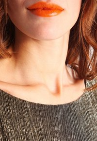 Metallinen, poimutettu yläosa, jossa on leveä kaula-aukko; kirkas oranssi huulipuna; luonnollinen ihonväri; pehmeät, aaltoilevat hiukset hartioiden ympärillä.