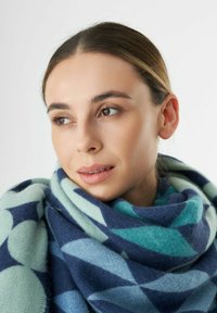 Wollen sjaal van een wolmix met een geometrisch patroon in marineblauw, lichtblauw en mintgroen, elegant om de hals gewikkeld.