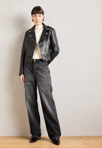 Zwarte nepleer bikerjack met zilverkleurige hardware, gecombineerd met high-waisted donkergrijze wijde jeans en zwarte puntige schoenen.
