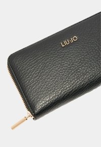 Must mustra nahkrahakott tekstuuriga viimistlusega, kuldse metallist riistvara ja "LIU-JO" logo ees. Omab kuldset luku sulgemist.
