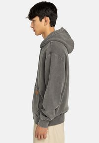 Sudadera de algodón gris con bolsillo tipo canguro, capucha con cordón y tejido texturizado. Presenta un pequeño parche de cuero en el bolsillo.