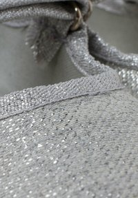 Chaussures gris clair avec une tige tissée texturée comportant des fils métalliques, une bordure lisse contrastante et un détail de lien décoratif.