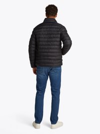 Sort puffjakke med høj krave, med quiltet tekstur og slim fit, iført med blå jeans og hvide sneakers.