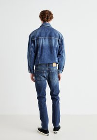 Jachetă din denim și blugi de culoare albastră medie, cu o croială lejeră, cusături contrastante și o pată din piele bej pe talie.