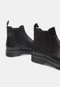 Bottines en cuir noir avec des panneaux élastiques sur les côtés, une semelle en caoutchouc texturée et des tirettes pour un enfilage facile. Fini lisse avec des coutures subtiles.
