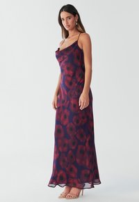 Šaty bez rukávů až na zem z průsvitné, lehké látky s tmavě fialovým základem a květinovým vzorem v červené a černé barvě.