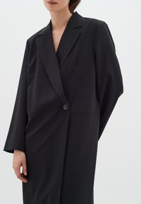 Juodas švarkas, pagamintas iš lygaus audinio. Yra išpjautas atlapas, vienas mygtukas ir priekinė kišenė. Per didelis, pritaikytas profilis su ilgomis rankovėmis.