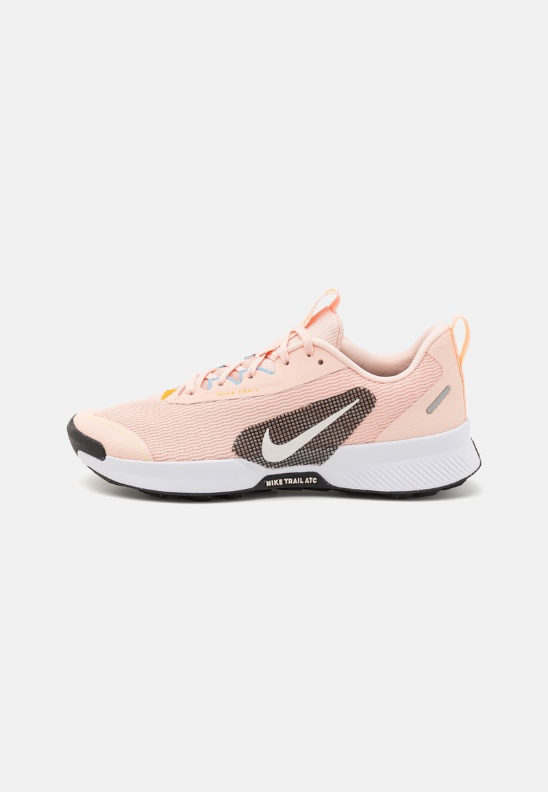 Chaussure de course Nike Trail ATC rose clair avec une semelle intermédiaire blanche, une semelle extérieure noire, un logo Nike blanc et une fermeture à lacets.