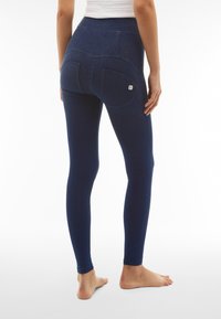 Leggings blu navy con vita alta, tessuto testurizzato e due tasche posteriori. Presentano cuciture a contrasto e un piccolo logo sul retro.