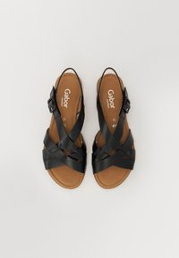 Black leather sandals with crisscross straps, adjustable buckle, and brown cushioned insole. Flat design suitable for casual wear.