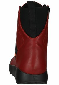 Botín de piel roja con panel lateral elástico negro, cremallera trasera y suela de goma negra, que presenta un acabado suave y un diseño minimalista.