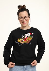 Felpa nera con un design a cartone animato di un personaggio su una slitta, circondato da regali, con un cappello rosso e bianco e un'espressione giocosa.
