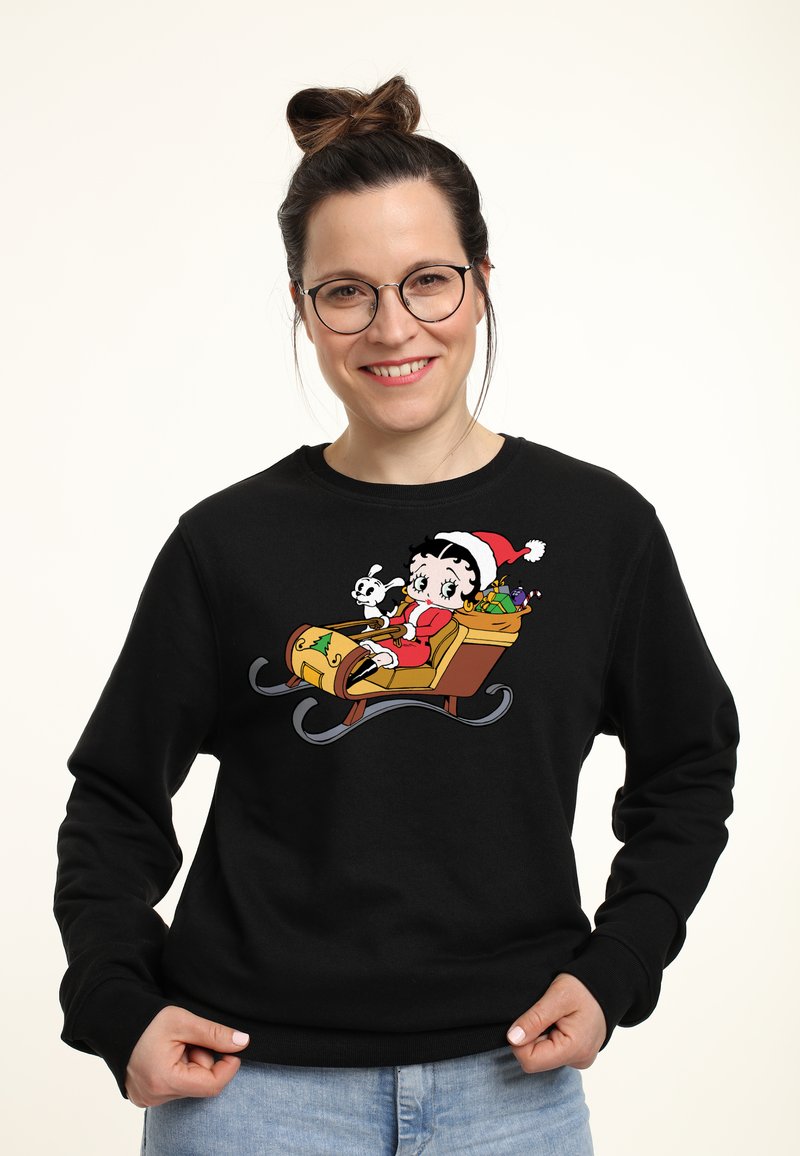 Felpa nera con un design a cartone animato di un personaggio su una slitta, circondato da regali, con un cappello rosso e bianco e un'espressione giocosa.
