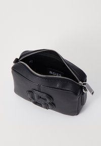 Borsa in pelle nera con finitura texturizzata, dotata di chiusura con zip e logo in rilievo. L'interno è foderato, rivelando un design semplice e funzionale.