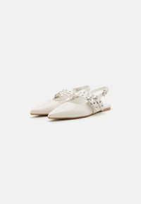 Chaussures slingback en cuir synthétique blanc avec un bout pointu et des sangles décoratives ornées de clous en argent. Semelle plate, design minimaliste.