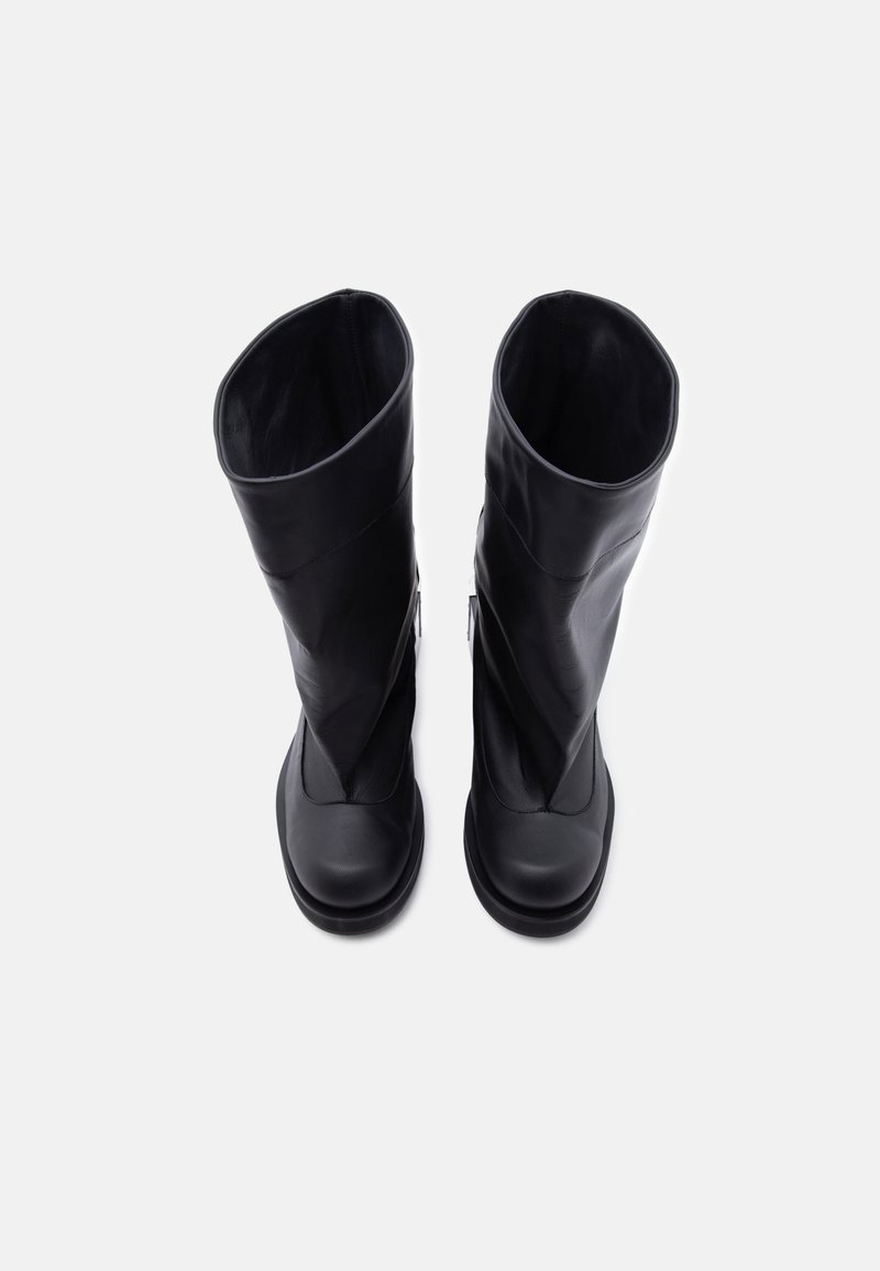 Coppia di stivali alti in pelle nera in piedi su sfondo bianco semplice, visti dall'alto.