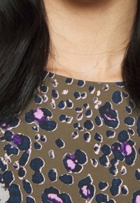 Lyhytsiureri, jossa on ruskea tausta ja leopardi-printti mustan, sinisen ja violetin sävyissä, sileä kangas.