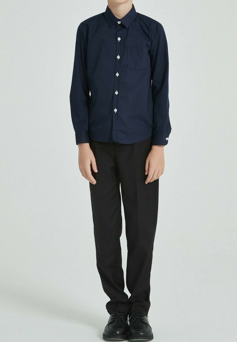 Chemise à manches longues navy avec un col pointu, poche avant et boutons blancs, associée à un pantalon droit noir et des chaussures noires.