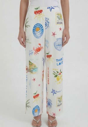 White wide-leg pants with colorful summer-themed prints including cherries, crabs, starfish, lemons, and coastal text, worn with silver sandals.