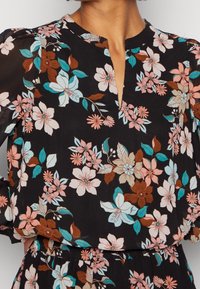 Robe noire à motif floral avec un décolleté en V, des manches longues bouffantes et une taille élastique. Fleurs roses, bleues et marron avec des feuilles.