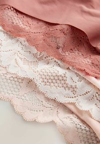 Țesături din dantelă în nuanțe de roz pal și roz deschis, cu modele complicate și margini ondulate, suprapuse peste o țesătură netedă și solidă.