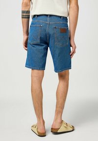 Blauwe denim shorts met een ontspannen pasvorm, voorzien van achterzakken en een leren label. De stof heeft een klassieke textuur en een lichte vervaging.