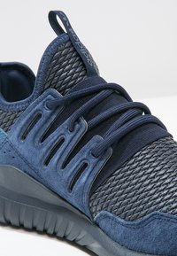 Scarpa da ginnastica blu con tomaia in mesh strutturato, dettagli in suede, lacci elastici e suola in gomma spessa con motivi scolpiti.