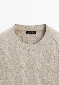 Pull léger beige à col rond, présentant un motif en côtes et des manches à bords ribbées. L'étiquette de la marque indique "Massimo Dutti", fabriqué en Chine.