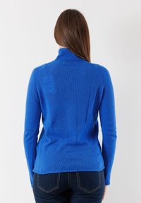 Maglione a collo alto lavorato a maglia blu con maniche lunghe, tessuto texturizzato e silhouette aderente, abbinato a jeans scuri.