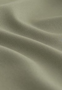 Green fabric with a soft, textured surface; features fine ribbing and smooth folds, creating depth and dimension in the material.