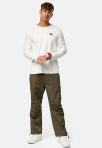 Langærmet hvid T-shirt med et sort logo på venstre bryst, parret med olivengrønne cargo-bukser og hvide sneakers.