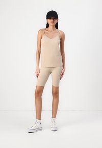 Beez värvi tank tops õhukeste rihmadega ja sobivad nahakleidid, mille juurde on kombineeritud valged kõrged spordijalatsid ja must pesapallimüts.