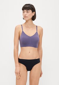 Soutien-gorge wireless viola con spalline sottili e rifiniture in pizzo, abbinato a mutande nere senza cuciture. Tessuto liscio con un design aderente.
