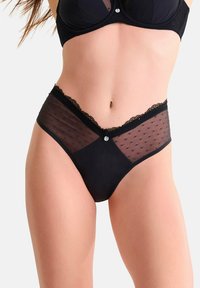 Culotte noire avec un design en maille transparente à pois, des bordures en dentelle et un petit détail décoratif à l'avant. Tissu lisse et coupe ajustée.