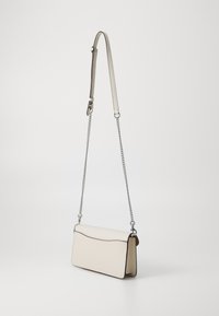 Crossbody bag in cream leather with a smooth texture, curved top edge, and silver chain strap. Features minimal stitching and sleek design.