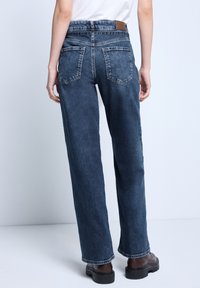 Jeans rectos de color azul oscuro con una cintura alta, cuatro bolsillos y una etiqueta de cuero en la parte trasera. Fabricados en denim con una textura suave.
