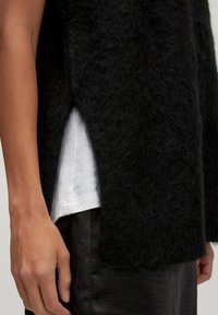 Black fluffy knit top with side slits, layered over a white shirt. The fabric appears soft and textured, paired with dark trousers.