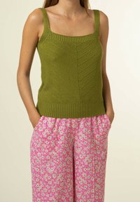 Olivgrön stickad tanktop med fyrkantig halsringning och strukturerat mönster, kombinerad med rosa byxor med blommönster och resårmidja.