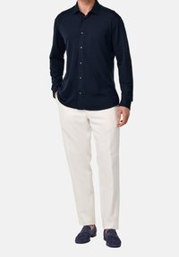 Námořnická košile s dlouhým rukávem a knoflíkovým zapínáním, krémové kalhoty a námořnické mokasíny s hladkým povrchem a klasickým střihem.