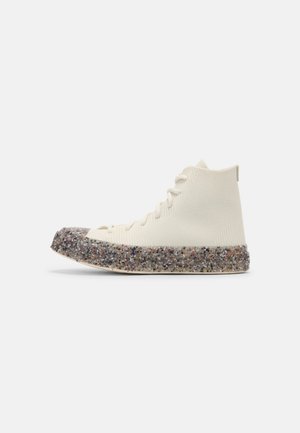 High-top sneaker met crème kleurige gebreide bovenkant en gevlekte grijze textuurs zool, afgebeeld in zijaanzicht tegen een witte achtergrond.