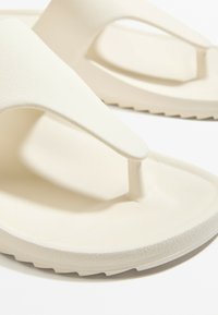 Fehér, textúrált gumiból készült flip-flop papucsok, thong dizájnnal, lapos, bordás talppal a jó tapadás és kényelem érdekében.