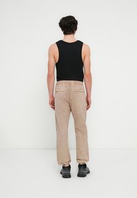 Ανδρικό άνε το παντελόνι σε μπεζ χρώμα με λεπτή υφή, ελαστική μέση και ριμπ τελείωμα. Μαύρο φανελάκι και μαύρα αθλητικά παπούτσια ολοκληρώνουν την εμφάνιση.