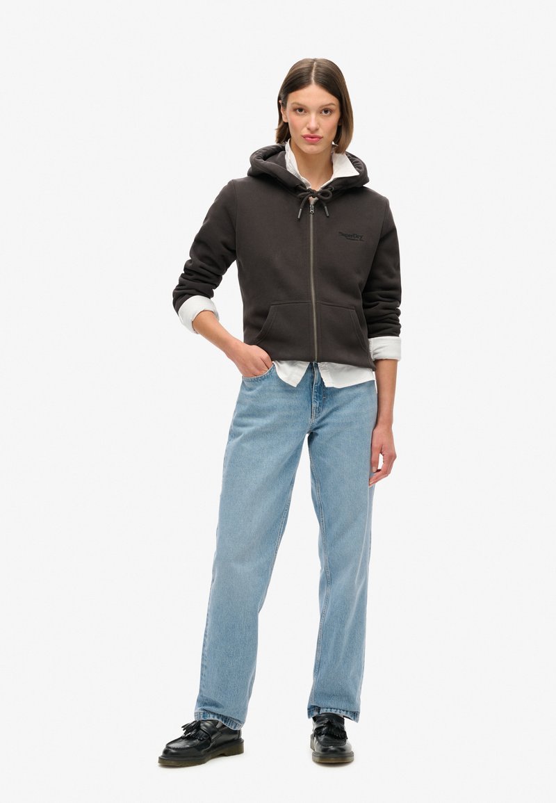 Schwarzer Zip-Hoodie mit Kordelzug, grauem Innenfutter und Logo. Kombiniert mit hellblauen, geraden Jeans und schwarzen Schuhen. Einfaches Design.